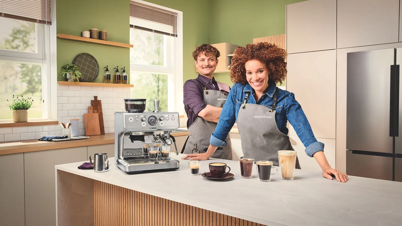 Двоє бариста за стільницею з еспресо-машиною Bosch HomeCafé Series 4 і чашками кави