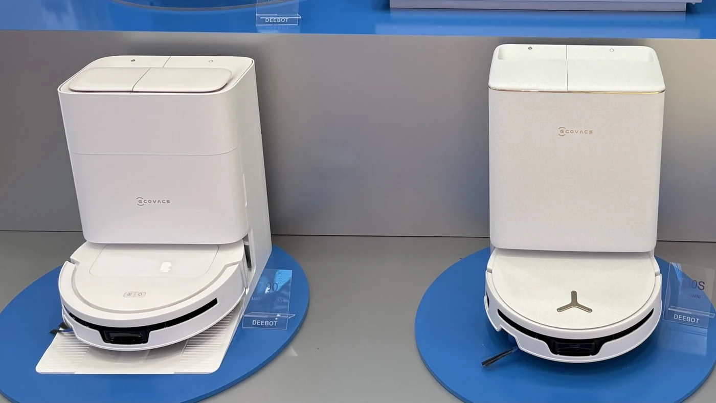 Роботи-пилососи ECOVACS DEEBOT T90 MAX PRO OMNI і T90S PRO OMNI на білих док-станціях із табличками моделей на стенді ECOVACS